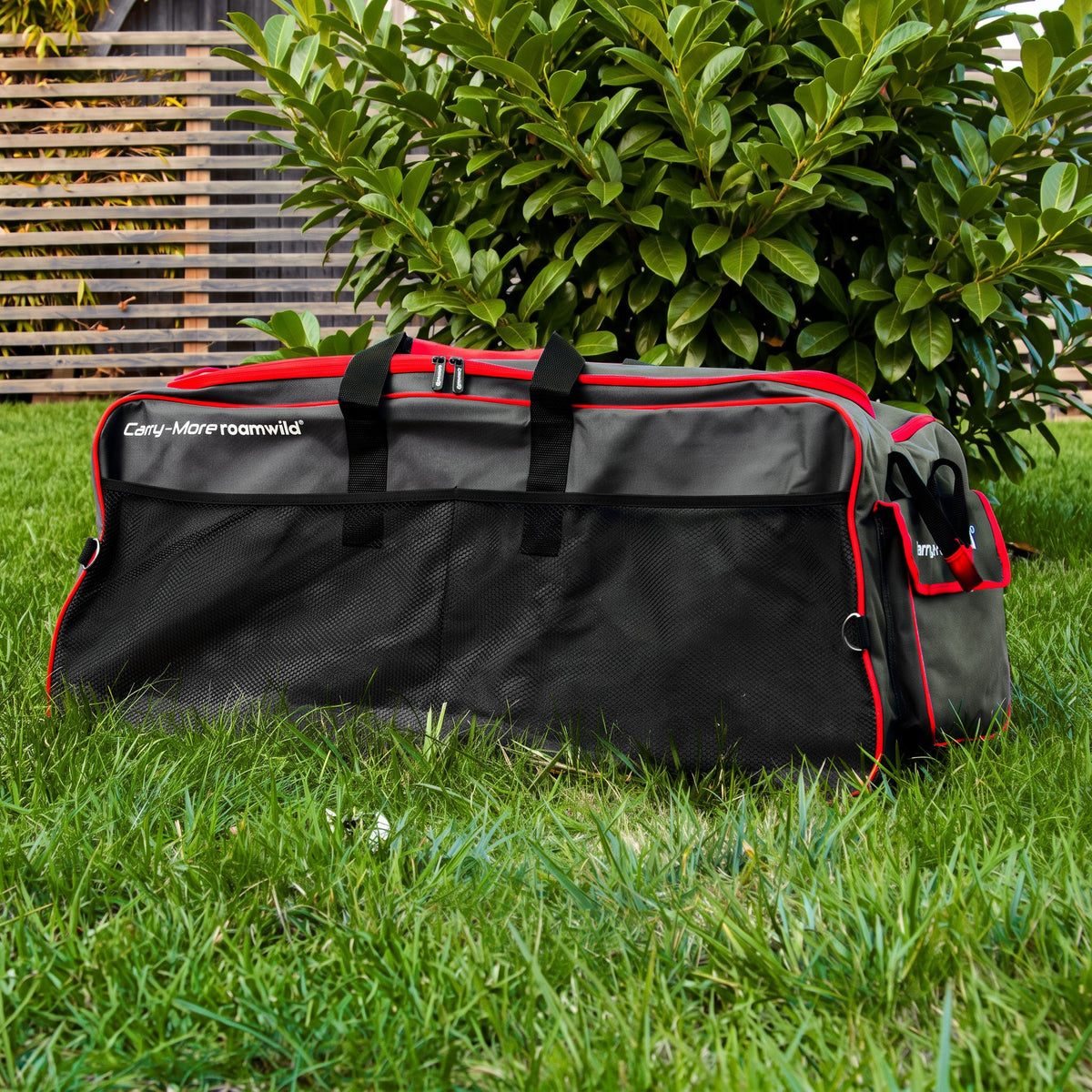 Grey and red Roamwild Carry-More wheeled bag on a garden lawn